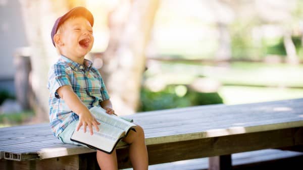 Little Boy Laughing While Reading the Bible Christian Stock Photo
